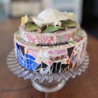 ceramic and glass with Staffordshire bone flowers Trachemys script turtle skeleton and spent bullet casings on press glass pedestal cake plate. 8-inch round.