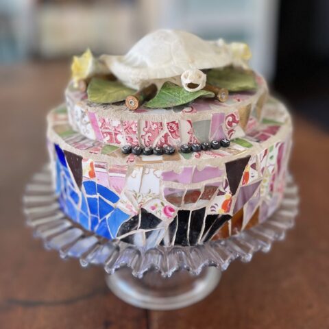 ceramic and glass with Staffordshire bone flowers Trachemys script turtle skeleton and spent bullet casings on press glass pedestal cake plate. 8-inch round.