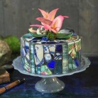 ceramic and glade with Capodimonte lily, qual egg, moss and mussel shell on vintage alabaster glass footed pedestal can plate. 8-inch round.